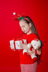 圣诞节微笑一个有趣的快乐女孩肖像头上缠着角绷带抱一只泰迪熊穿着圣诞睡衣背景为鲜红色头抱着一只泰迪熊与鲜红色背景隔开指点图片