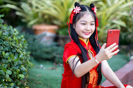 身着传统红潮相香装饰的可爱亚洲小女孩在神庙新年节举行自拍带智能手机的新年节时自信的幸福愉快图片