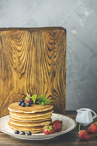 美味的烤瓷炉小陶罐子上浅木制桌和灰色底的糖浆煎饼中含有白莓蓝和薄荷甜的目图片