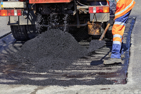 基辅建筑工人道路服务在修建和补公路期间用新的沥青铲起道路工人分发一块沥青并配有铁铲用于修补公路工业的图片
