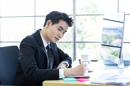 公司的男人浓度充满欢乐的心情一个来自亚洲年轻商人的欢乐情绪有想法使人们注意到成功的商业计划在笔记本和电脑上取得成功在办公室的木制图片