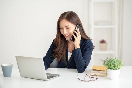 中小企业美丽的亚洲女商人在办公室通过手机与客户交谈在办公室使用手机积极的电子商务图片
