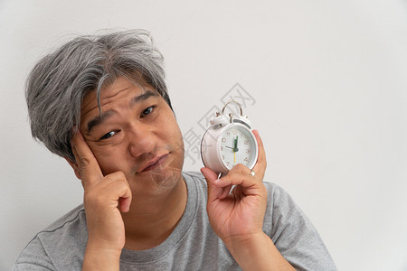 亚洲中年人举着一个白色闹钟脸闷不乐感觉很舒服他的问题是睡眠紊乱失是痛苦的念头无聊遭受成人图片