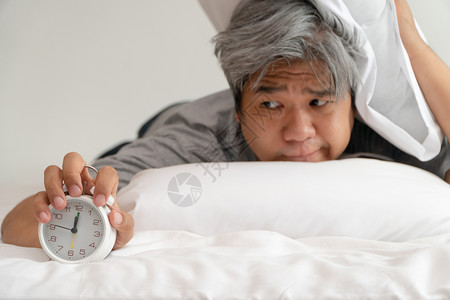 成人亚洲中年举着一个白色闹钟脸闷不乐感觉很舒服他的问题是睡眠紊乱失是痛苦的念头遭受卧室图片