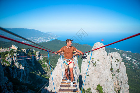 小路旅行悬崖在山上吊桥的年轻勇敢男子跨越绳桥上的裂缝男子图片