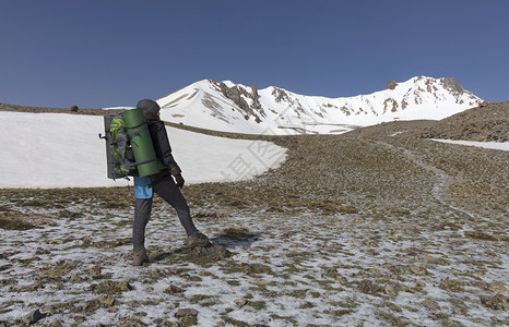 一位背着着一个的旅游妇女手里拿着一个追踪棒前往雪地高山进行一场运动游客从山上爬到雪地顶峰登山者一种远足图片