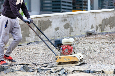 袖珍的压实机一种名道路工人使用汽油炉灶在道路修理工地压碎石块随后铺设路面的板块建筑工人用汽油振动压缩机粉碎石头随后铺设路面的板块图片