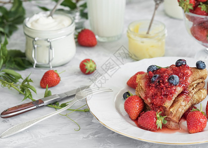 美食加果酱的煎饼放在白板上盘子的煎饼周围是新鲜的浆果旁边是一杯牛奶和酸油加早餐收紧桌子上装饰着一个常春藤枝草莓早晨图片