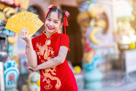 美丽身着红色传统长相装饰的可爱亚洲小女孩手拿着黄信封准备在神庙举办新年庆典她戴着黄包幸运的钱图片
