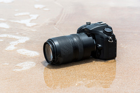 远程在极端环境中旅行和试验时摄影师DSL用DSR摄像机在水海浪的滩上打湿时使用带长光镜头的DSLR照相机进行防水测试损坏的信号图片