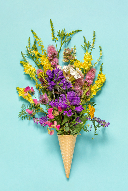 有创造力的女好蓝纸背景上华夫饼冰淇淋蛋筒中的花束场彩色朵妇女节或母亲图片