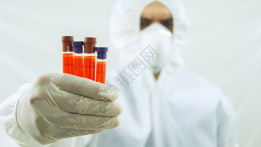 科学红色的颜戴面罩和白生物防护服的医手臂向前伸右拿着4个试管前景是白色背的血样上的前图片