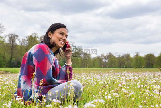 坐在开花草地的哥伦比亚女人用手机打来电话荷兰语懒惰接触图片