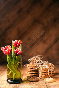 木头简单质朴的静物绿色玻璃中盛开的红色郁金香在深木桌上堆放各种饼干美术质朴背景面包店甜点图片
