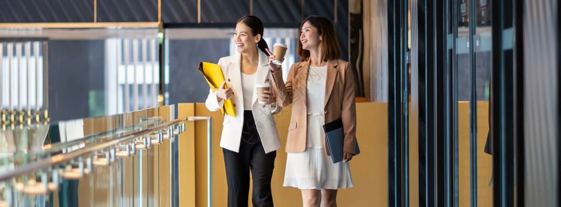 有创造力的女士在现代办公室或合用空间的咖啡休息放松和谈话商业人际伙伴关系概念期间两名亚洲女商人在咖啡休息期间行走和说话休闲聊天商图片