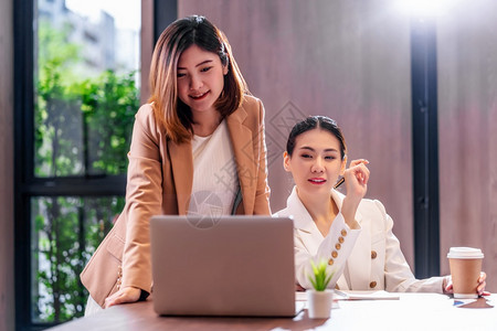 讨论在现代会议室办公或工作空间咖啡休息伙伴和同事概念中通过技术笔记本电脑与伙伴企业合作的两名亚洲女实业商人幸福高级的图片