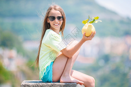 意大利语象征阿马尔菲海岸背景的小女孩在地中海和天空背景中手握着大黄柠檬在海洋和天空背景下旅游的图片
