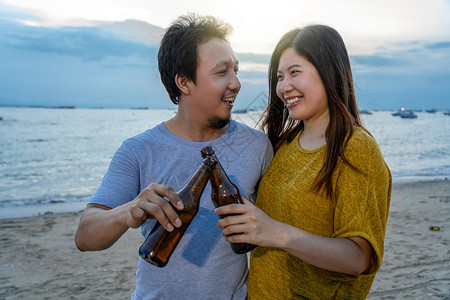 团体几个亚裔快乐的朋友在海滩上喝着派对饮料和欢乐啤酒瓶当日落时间庆祝和放松当与爱人度假时的情侣概念幸福跳舞图片