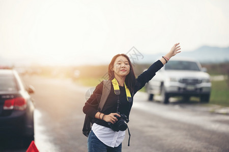 常设红色的亚洲青年妇女背着包徒步旅行在汽车撞后压力过重公路上有一辆汽车的红色三角地带妇女在路边站着举起手来保险图片