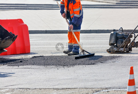 明亮的建造采用道路工人身穿明橙色长裤在路的围栏下停工区修补有热沥青和坡道的坑洞并配有汽油振动板道路工人身穿明橙黄色长裙新鲜沥青木图片