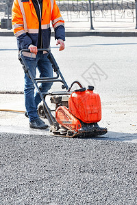 建造压力人行道身穿明橙色反射夹克的公路工人使用振动板在道路修理工点将沥青压缩成垂直图象复制身穿橙色夹克的公路工人用一个带汽油振动图片