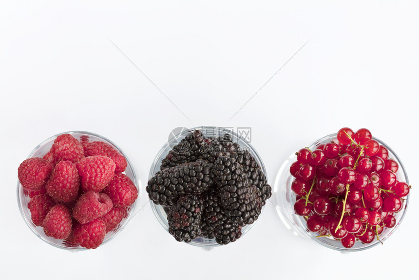 站立果味黑莓大和红沙律被倒入透明的拿铁杯中在光背景上排成一高键Raspberry的图像大黑莓和红草原以光背景置于清晰的玻璃里一个图片