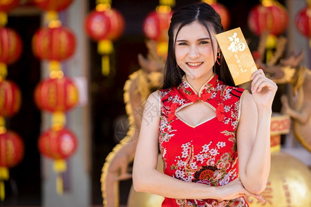礼物为了身着红色传统青山装饰的亚裔年轻女子手拿着黄信封在泰国中华神庙举办新年庆典节上展示新年节包图片