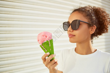 甜的一种穿着白色T恤衫和轻牛仔裤的年美籍非裔女孩在阳光日吃冰淇淋有选择地关注小重点领域食物图片