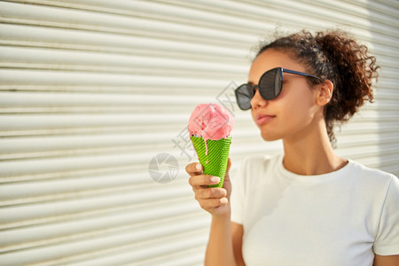 穿着白色T恤衫和轻牛仔裤的年美籍非裔女孩在阳光日吃冰淇淋有选择地关注小重点领域太阳请享用非洲人图片