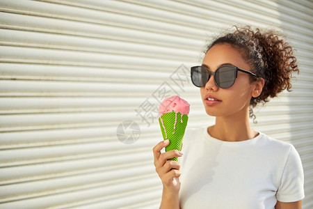 可选择的乐趣穿着白色T恤衫和轻牛仔裤的年美籍非裔女孩在阳光日吃冰淇淋有选择地关注小重点领域非洲人图片