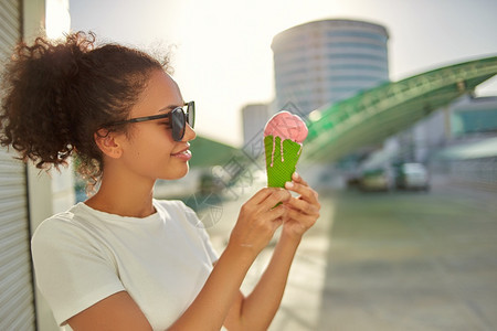 穿着白色T恤衫和轻牛仔裤的年美籍非裔女孩在阳光日吃冰淇淋有选择地关注小重点领域女可口日落图片