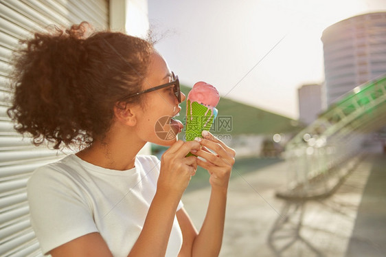 穿着白色T恤衫和轻牛仔裤的年美籍非裔女孩在阳光日吃冰淇淋有选择地关注小重点领域夏天白色的甜点图片