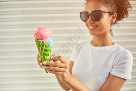 幸福穿着白色T恤衫和轻牛仔裤的年美籍非裔女孩在阳光日吃冰淇淋有选择地关注小重点领域食物笑图片