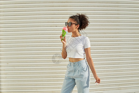 穿着白色T恤衫和轻牛仔裤的年美籍非裔女孩在阳光日吃冰淇淋有选择地关注小重点领域可口时髦的奶油图片