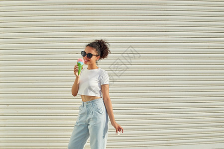 卷曲时髦的美国人穿着白色T恤衫和轻牛仔裤的年美籍非裔女孩在阳光日吃冰淇淋有选择地关注小重点领域图片
