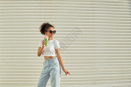 幸福甜的穿着白色T恤衫和轻牛仔裤的年美籍非裔女孩在阳光日吃冰淇淋有选择地关注小重点领域日落图片