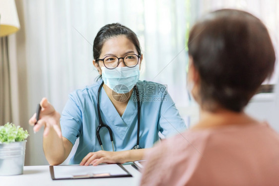 生活健康身穿蓝色制服和保护面罩的亚洲女医生向院执业师高级女病人提供戴眼镜和外科面具的建议以撰写处方信息的在医院开业师身上戴眼镜和图片