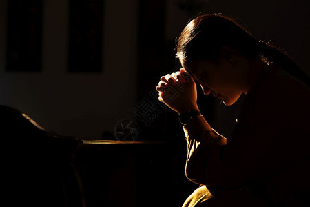 女坐在低轻光教堂和祈祷国际人权日概念的压抑妇女在低光下教堂和祈祷孤独挫折图片