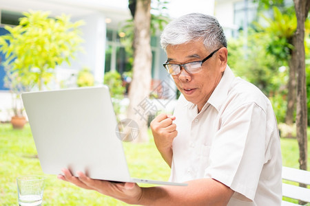 震惊课程一名年长的亚洲老人拿着电脑笔记本在得到子邮件后惊讶地读到院关于退休没有年龄主义和嗜好的概念消息AhnicationofN图片