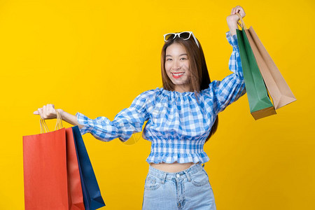 时尚购物者积极的迷人亚洲微笑年轻女在孤立的黄色背景复印空间和工作室黑色星期五季节销售概念中携带购物袋图片