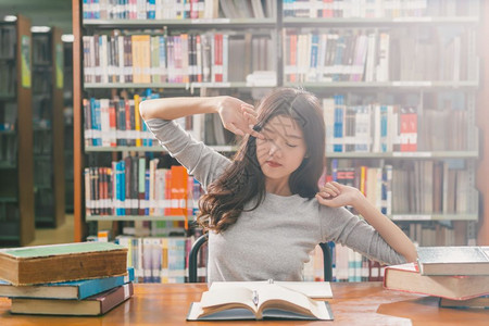 在大学图书馆或群落里阅读和做功课的亚洲青年学生在书架上木制桌子的各种书籍和文具上写着返回学校的书架习人们成图片