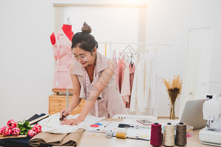 工作室厂在家庭办公室讲习班上工作的有吸引力亚洲时装设计师女时装设计师在家庭办公室工作时尚妇女创造新的布料设计汇编裁缝和纫衣服图片