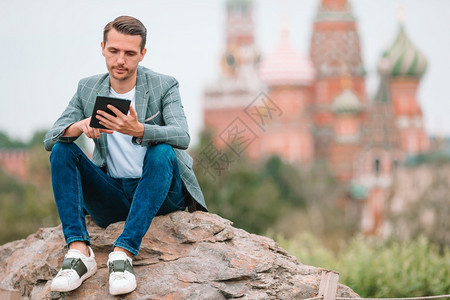 学生年轻的经理在圣巴西尔斯教堂和克里姆林宫肖像背景上有电话户外的青年男子莫斯科快乐城市青年男子欢乐在欧洲市商人的克里姆林宫肖像图片