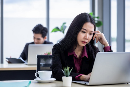 沮丧的伤心年轻亚洲商业女在工作场所用办公室工作人员笔记本电脑工作时对办公室后面的工作同事感到不满意的心理压力这些精神与办公室工作图片