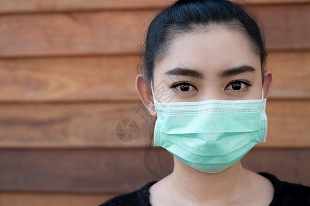 绿色紧贴近身的亚洲年轻妇女戴上医疗面罩以防止呼吸道疾病如在壁木背景上的流感摄像头19PM25粉尘和烟雾筛选健康图片