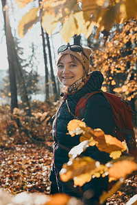 中间冒险旅游在秋天阳光明媚的白带着背包在森林里游荡的女人露天阳光晴朗的夜晚站在中年活跃女视野前积极花着闲暇时间走在林道上树木间有图片