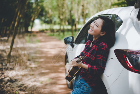 肖像假期唱歌与Ukulele在白色汽车附近的Ukulele一起在户外夏天微笑和玩乐的亚洲美女旅行摄影家Histster风格的概念图片