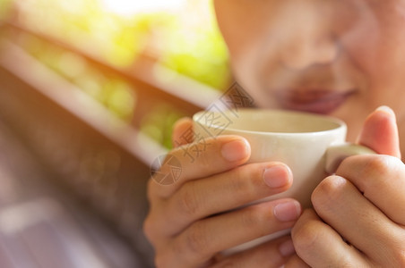 存在亚洲人热的握着咖啡杯手贴紧等待一位亚裔妇女在清晨轻光嘴唇上喝咖啡前举行图片