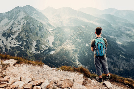 假期背着包在山上徒步旅行的年轻人积极度过暑假站在山顶欣赏景全的人后视图公园风景图片