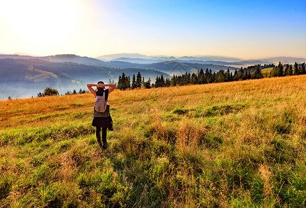远足一位年轻女在清晨太阳升起的光线下呼吸野生草药和花朵的芳香在山坡草原上迎来黎明并看着迷雾中的喀尔巴阡山脉年轻女在日出时喀尔巴阡图片